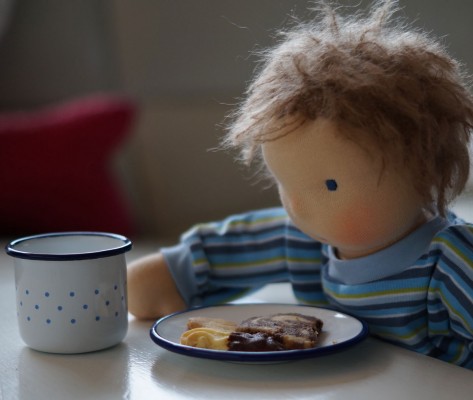 Waldorfpuppe sitzt am Tisch mit einem teller voller Weihnachtsplätzchen und einer Tasse Kakao