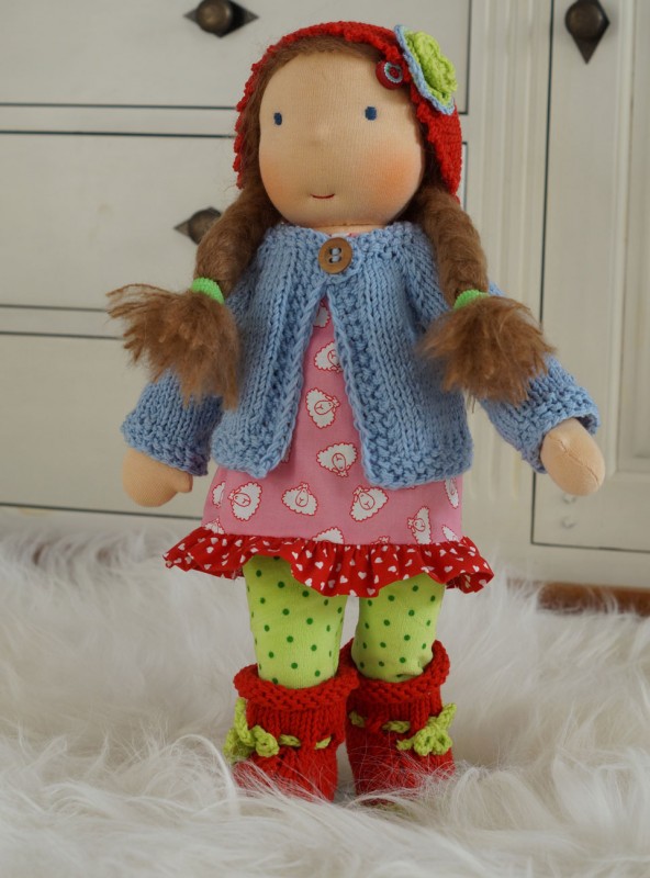 Puppe Waldorf Art nach Kundenwunsch Waldorfpuppe mit dunkelblonden Zöpfen trägt ein rosa Kleid mit kleinen Schäfchen drauf, dazu eine hellgrüne Leggins mit Punkten und roten Strickstiefelchen, hellblauer Stricljacke und Häkelmütze mit Blümchen