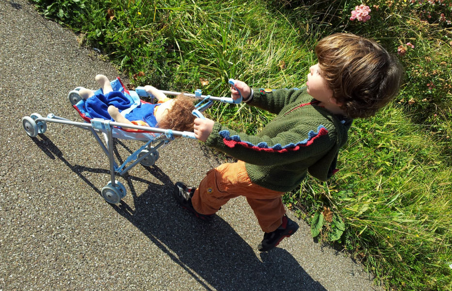 Junge fährt seine Puppe spazieren - Puppen für Jungs kleiner Junge kuschelt mit einer Babypuppe aus Stoff
